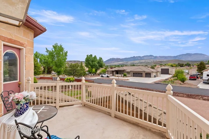 Stone exterior with an arched entry door, concrete patio, white railing, and mountain backdrop