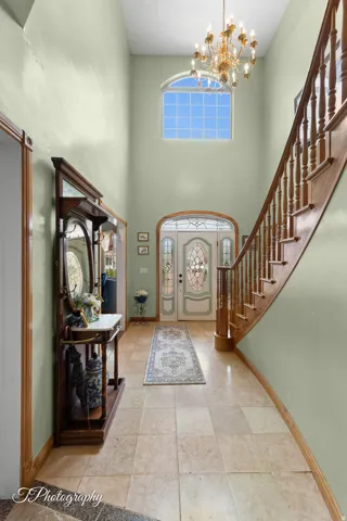 Grand foyer featuring a soaring vaulted ceiling with natural light from transom window, elegant chandelier, and wide-plank stone flooring