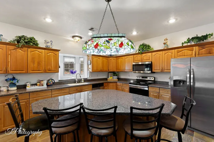 Chef's kitchen featuring warm wood cabinetry, stainless steel appliances, and a spacious island with seating for three