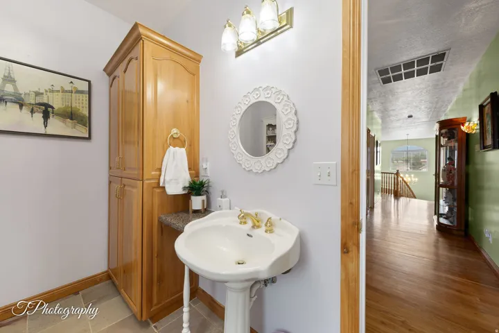 Pedestal sink with brass-finish fixtures, full-height wood-finish cabinetry, vanity lighting, and a decorative mirror