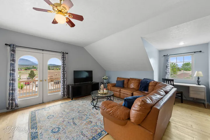 Hardwood-style flooring, arched French doors leading to a balcony, a ceiling fan with integrated lighting, a window with exterior scenery, and light-colored walls