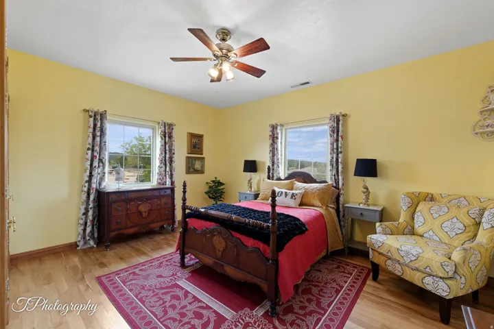 Bright, sun-filled bedroom with cheerful yellow walls, hardwood flooring, and dual windows with natural light