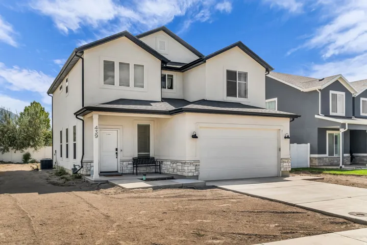 Stucco exterior with stone accents, covered entry, attached garage, concrete driveway, and gravel landscaping