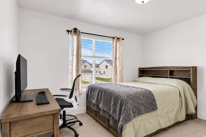 Recessed ceiling light fixture, white walls, carpeted flooring, window with blinds, and a built-in wooden headboard with shelving