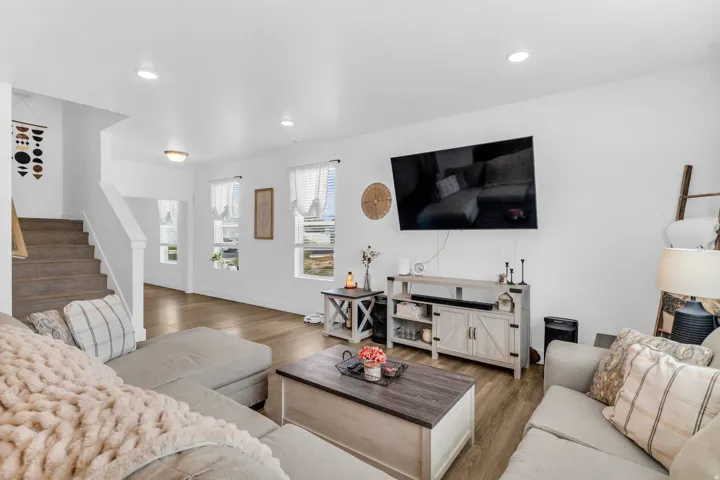 Recessed ceiling lighting, wood-finish flooring, white walls, multiple windows, and a staircase with white railings