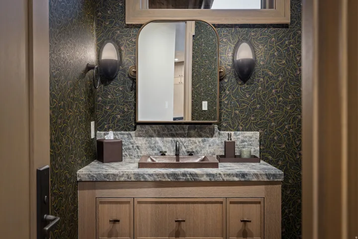 Vanity with stone countertop, integrated sink, wall-mounted sconces, and wood-finish cabinetry