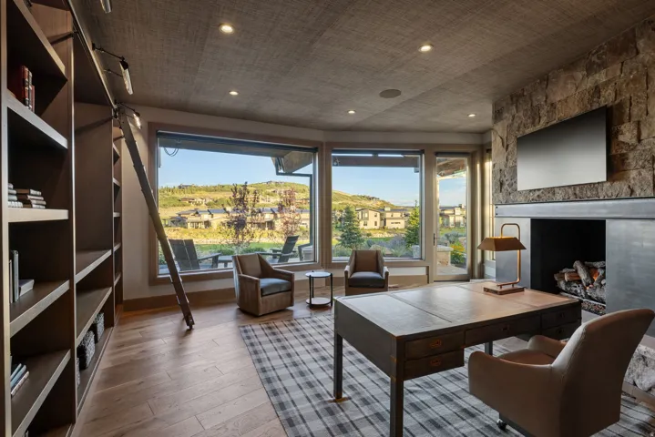 Stone-clad fireplace with a recessed hearth, integrated media niche, wood-finish flooring, and expansive windows