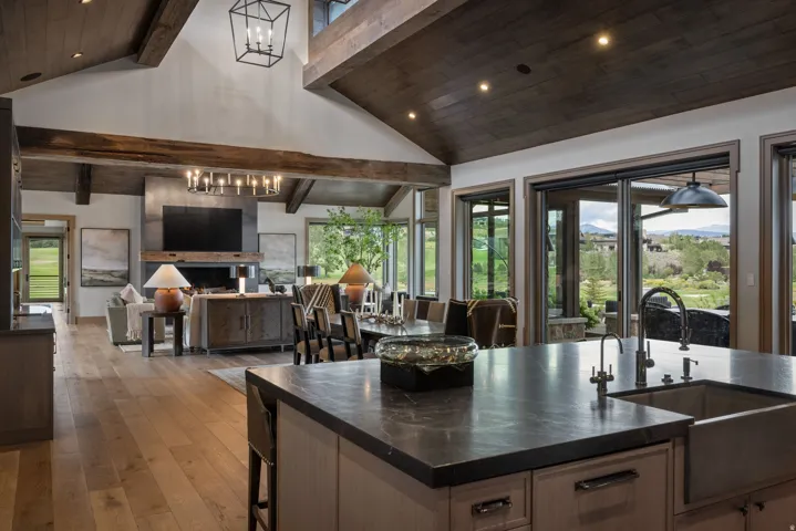 Vaulted wood-paneled ceilings with exposed beams, wood-finish flooring, a kitchen island with sink and dark countertop, and large glass sliding doors revealing distant scenery