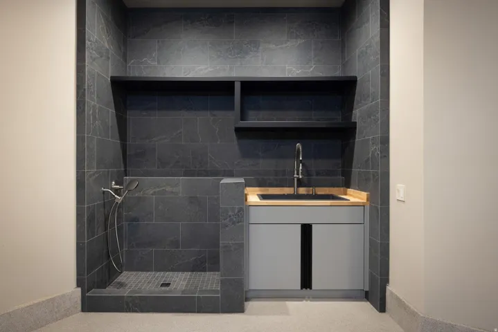 Tiled wash station with a handheld shower fixture, built-in shelving, and a cabinet with an integrated sink