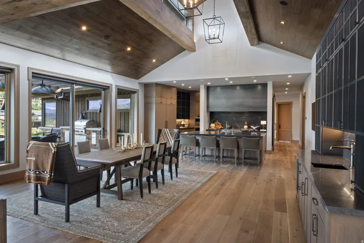 Vaulted wood-paneled ceilings with exposed beams, wood-finish flooring, sliding glass doors, dark kitchen cabinetry, and an expansive kitchen island