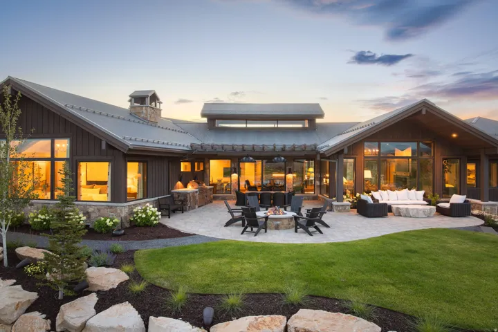 Expansive stone patio with built-in fire pit, multiple seating areas, and a stone-clad outdoor kitchen