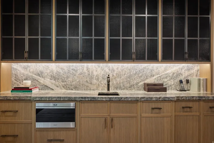 Custom cabinetry with wire mesh doors, stone countertops, integrated sink, stone backsplash with integrated lighting, and a built-in microwave drawer