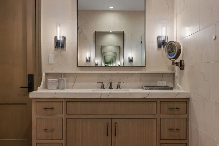 Wood-finish vanity with drawer and cabinet storage, under-mount sink, stone countertop, and two wall-mounted sconces