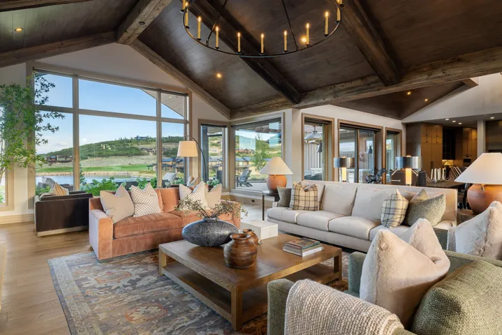 Vaulted wood-beamed ceiling, full-height window wall, light wood-finish flooring, and a large central chandelier