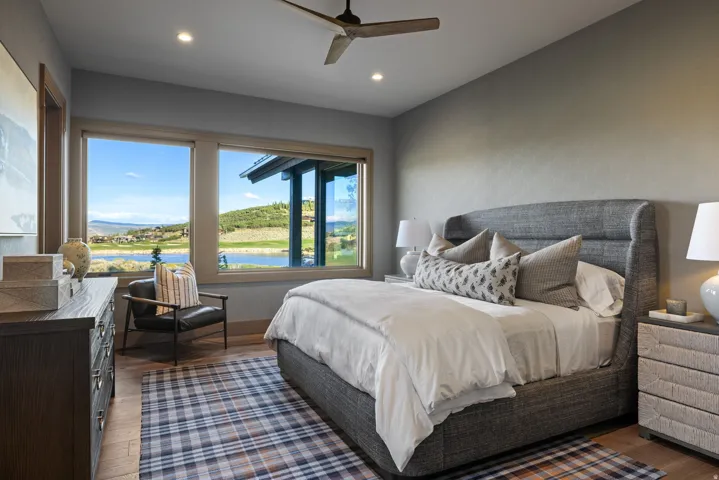 Expansive windows with mountain and lake scenery, light wood-finish flooring, recessed lighting, ceiling fan, and built-in dresser