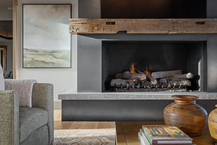 Contemporary living space featuring a striking linear fireplace with a wood-finish mantel and dark surround, wide-plank wood-finish flooring, neutral upholstered seating, and curated décor accents including ceramic vessels and framed artwork