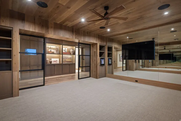 Wood-plank ceiling with recessed lighting and a ceiling fan, full-height mirrored wall, built-in shelving, glass-paned double doors, and light-toned carpeting