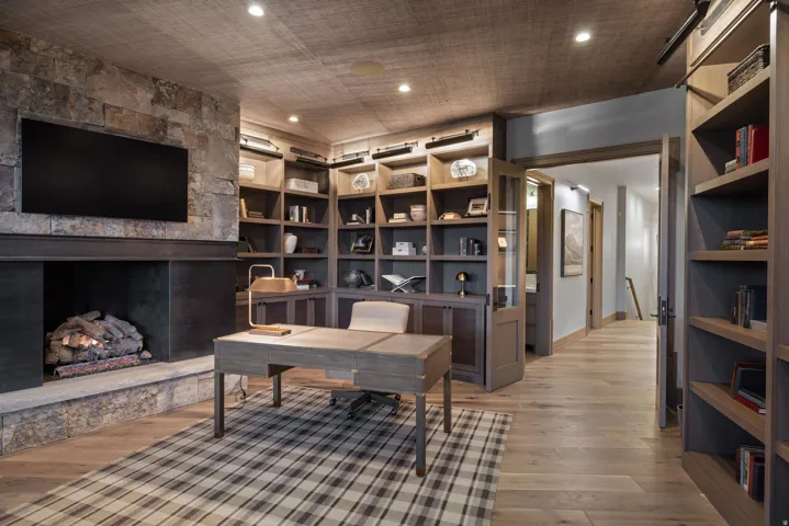Stone-clad fireplace with a dark wood mantel, built-in shelving, wood-finish flooring, and recessed ceiling lighting