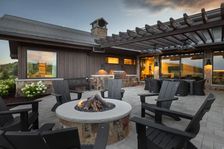Paver patio featuring a built-in fire pit, stone-clad outdoor kitchen with grill, and wood pergola with outdoor lighting