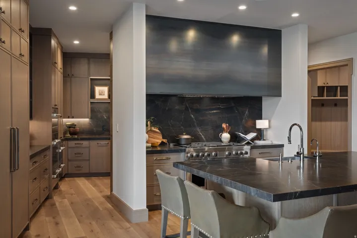 Integrated stainless steel appliances, dark stone countertops, wood-finish flooring, custom wood cabinetry, and a large central island with an undermount sink