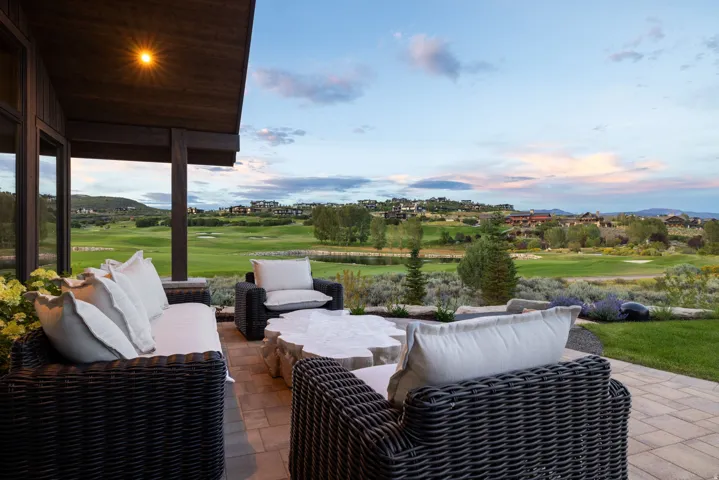 Covered patio with paver stone flooring, a dark wood ceiling, and a prominent golf course backdrop