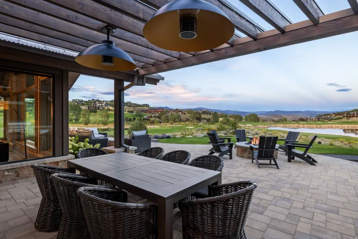 Expansive paver patio with a wood pergola, built-in fire pit, and adjacent water feature