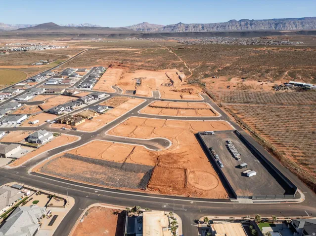 Expansive land parcel featuring developed roadways, surrounding residential structures, and distant mountainous terrain
