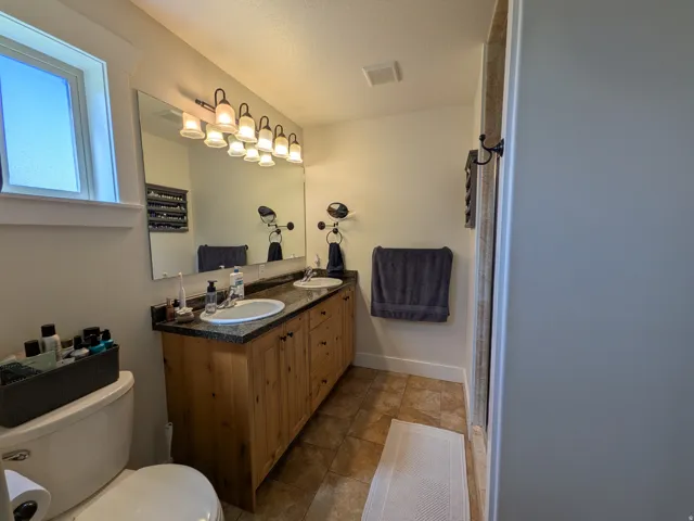 Master Bathroom featuring a Double vanity with granite-style countertop, dual undermount sinks, and wood-finish cabinetry