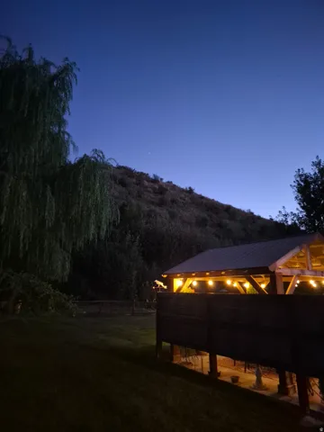 Expansive lawn area with a multi-level wood-clad structure, featuring a pitched roof and visible string lighting