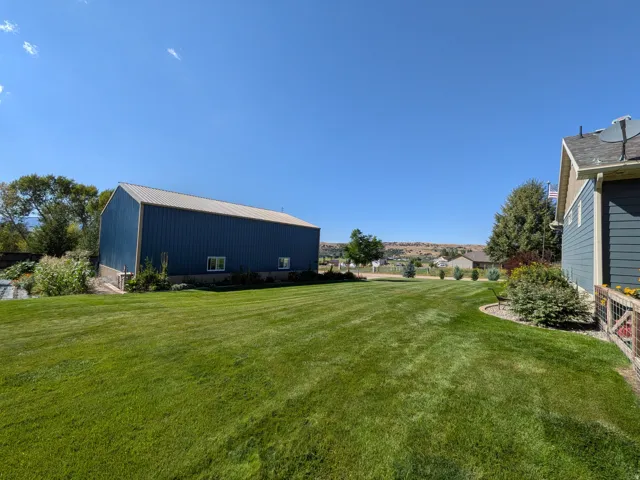 Expansive green lawn, blue metal-sided outbuilding with a metal roof, and established landscaping