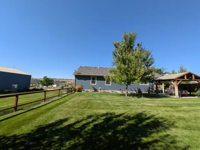 Expansive lawn with mature trees, a wooden gazebo, and a split-rail fence