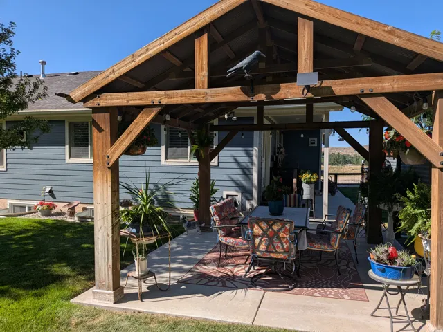 Covered patio with a wood beam pergola and string lighting, complemented by a manicured lawn and siding exterior