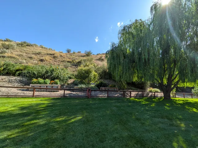 Expansive lawn area with a mature weeping willow tree, wood rail fencing, and tiered landscaping