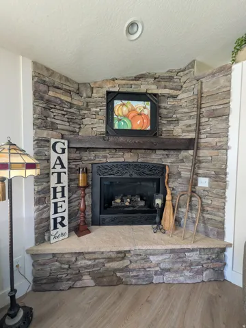 Stone-clad corner fireplace with a substantial hearth, dark wood mantle, and wood-finish flooring