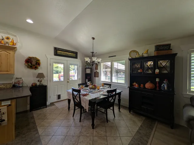 Vaulted ceiling with recessed lighting, tile flooring with wood-finish inlay, double glass-panel doors, kitchen cabinetry with dark countertop, and plantation shutters