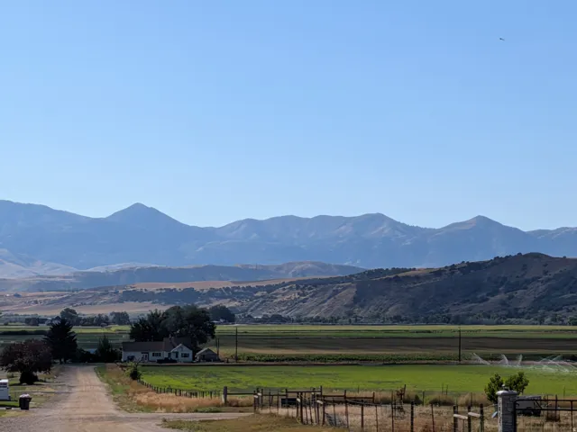 Expansive rural property featuring a single-story dwelling, surrounding fields, and distant mountain ranges