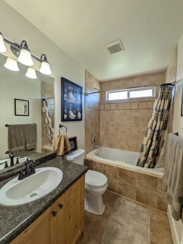 Tile-surround bathtub and shower combination with a window, single vanity with integrated sink, wood-finish cabinetry, and tiled flooring