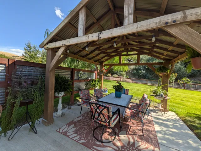 Covered outdoor living space featuring a wood-beam gazebo with a corrugated metal roof, concrete patio, and fenced perimeter