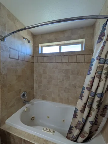 Jetted bathtub with tiled surround, chrome fixtures, and upper window