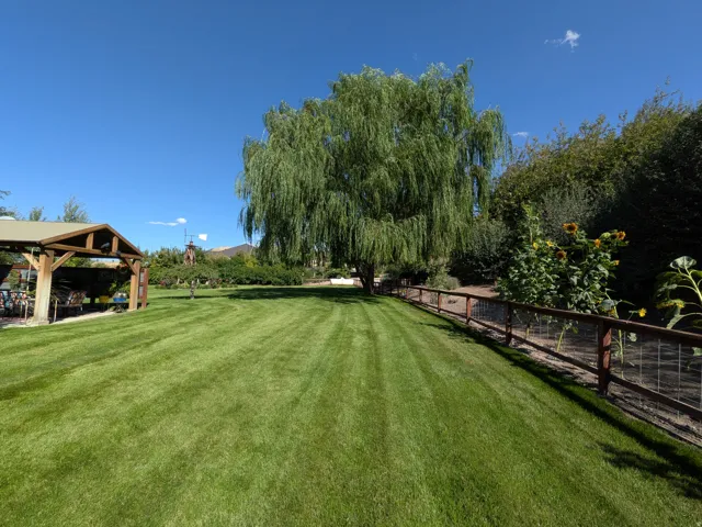 Expansive lawn featuring a mature willow tree, a covered gazebo, and a perimeter fence