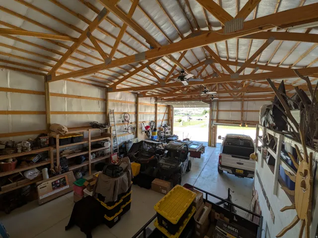 Expansive interior space featuring exposed wood beam ceiling, multiple ceiling fans, and a large roll-up door