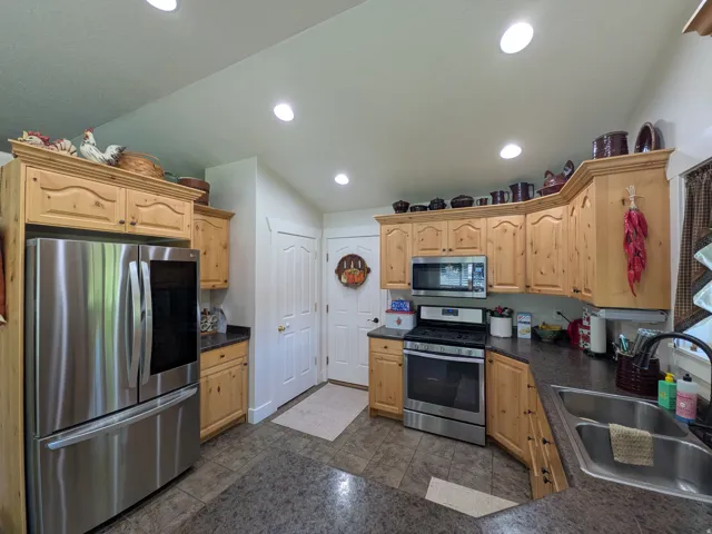 Natural wood cabinetry, stainless steel appliances, dark countertops, tile flooring, and recessed ceiling lighting
