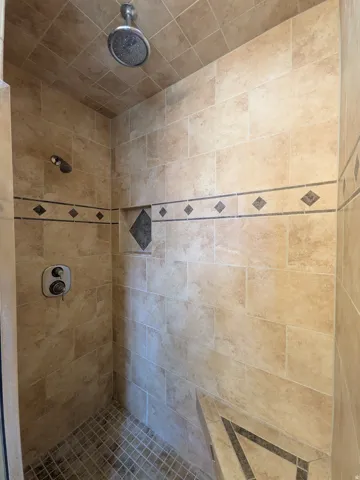 Master Tiled shower with a rain shower head, hand-held shower, built-in bench, and decorative accent tiles