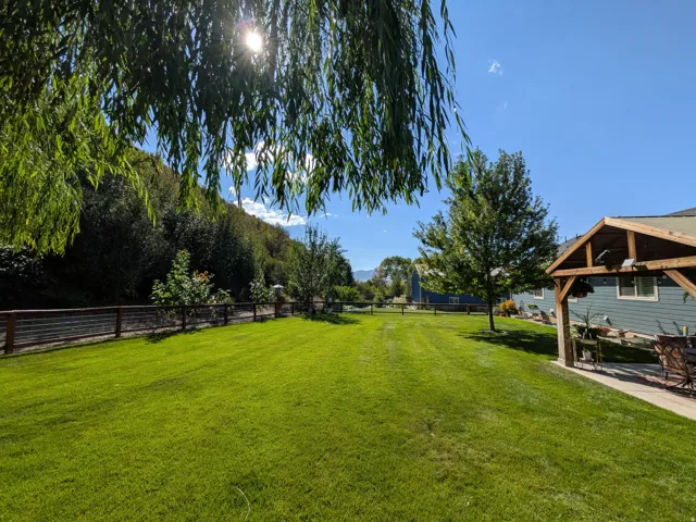 Expansive green lawn, wood-toned perimeter fencing, mature trees, and a covered outdoor patio structure