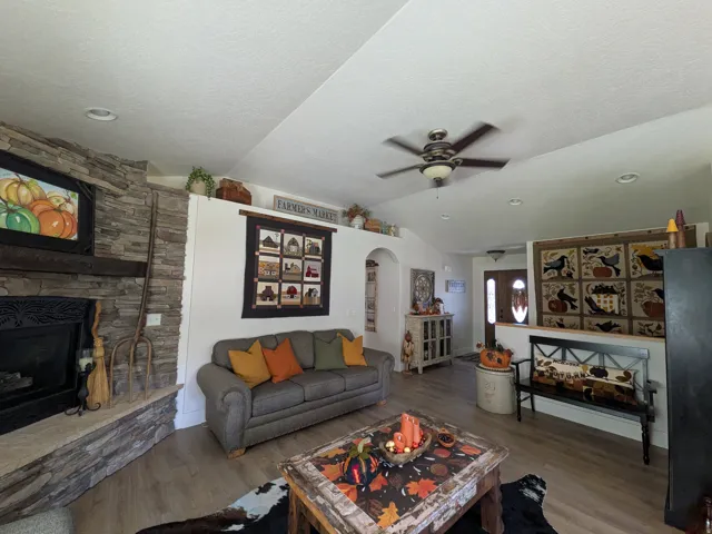 Vaulted ceilings with recessed lighting, stone-clad fireplace with mantel, wood-finish flooring, ceiling fan, and an arched entry