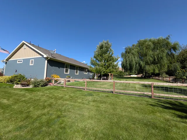 Expansive backyard featuring a manicured lawn, mature trees, and a split-rail fence