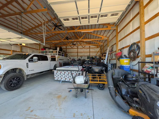 Spacious garage with multiple overhead doors, exposed wood beam ceiling, concrete flooring, and ceiling fans
