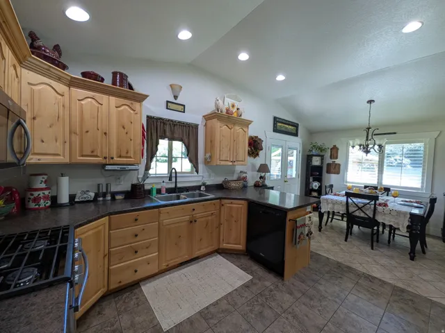 Vaulted ceiling with recessed lighting, wood cabinetry, built-in dishwasher, black countertops, and a dining area with a chandelier