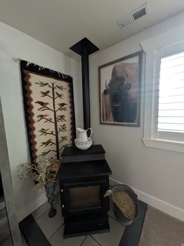 Black freestanding stove with a black stovepipe, and a window with blinds