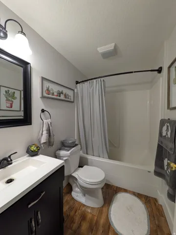 Bathroom featuring a white vanity with integrated sink, dark wood-finish flooring, a white bathtub with shower, and a white toilet